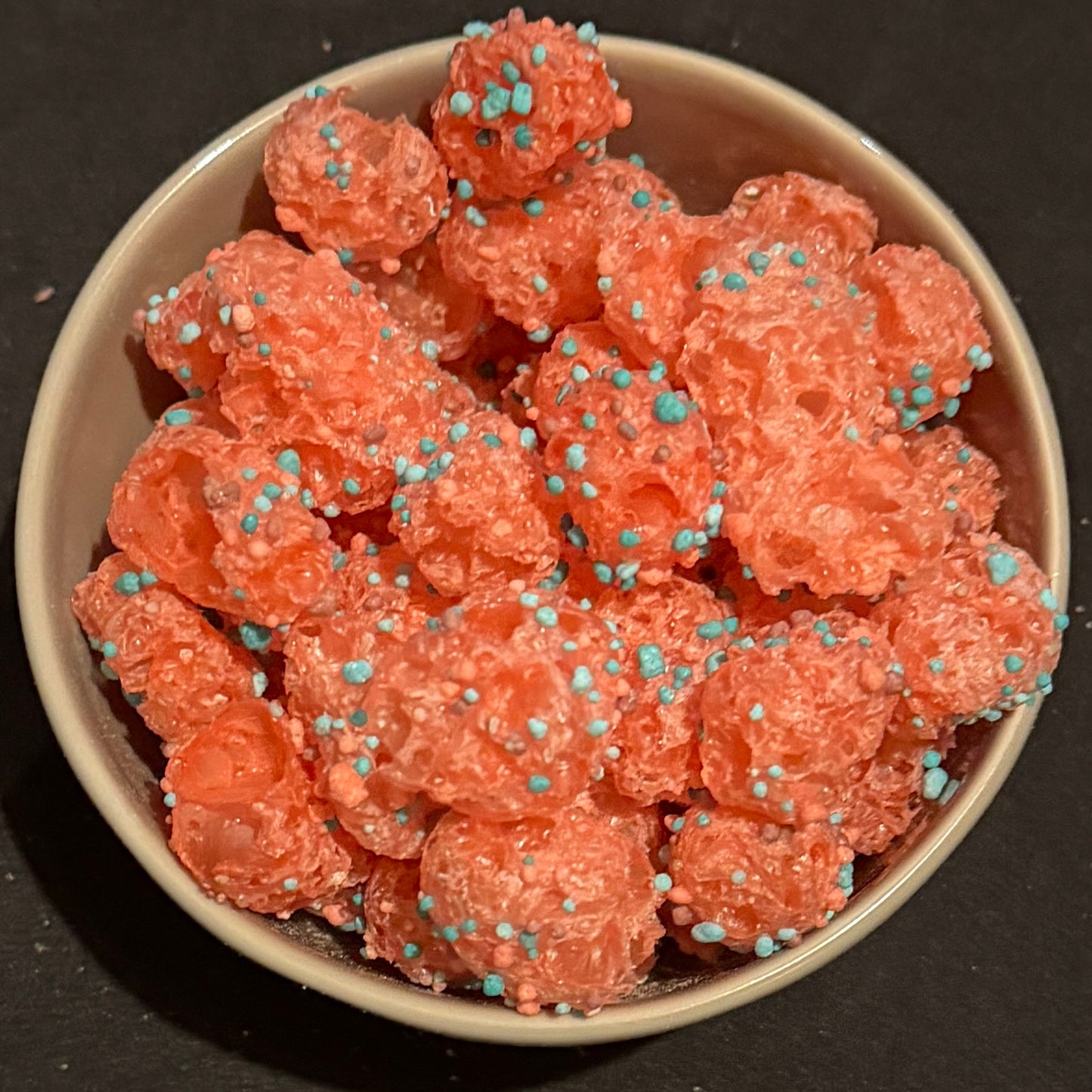 Pink nerd clusters freeze dried with blue nerds in a dark grey bowl