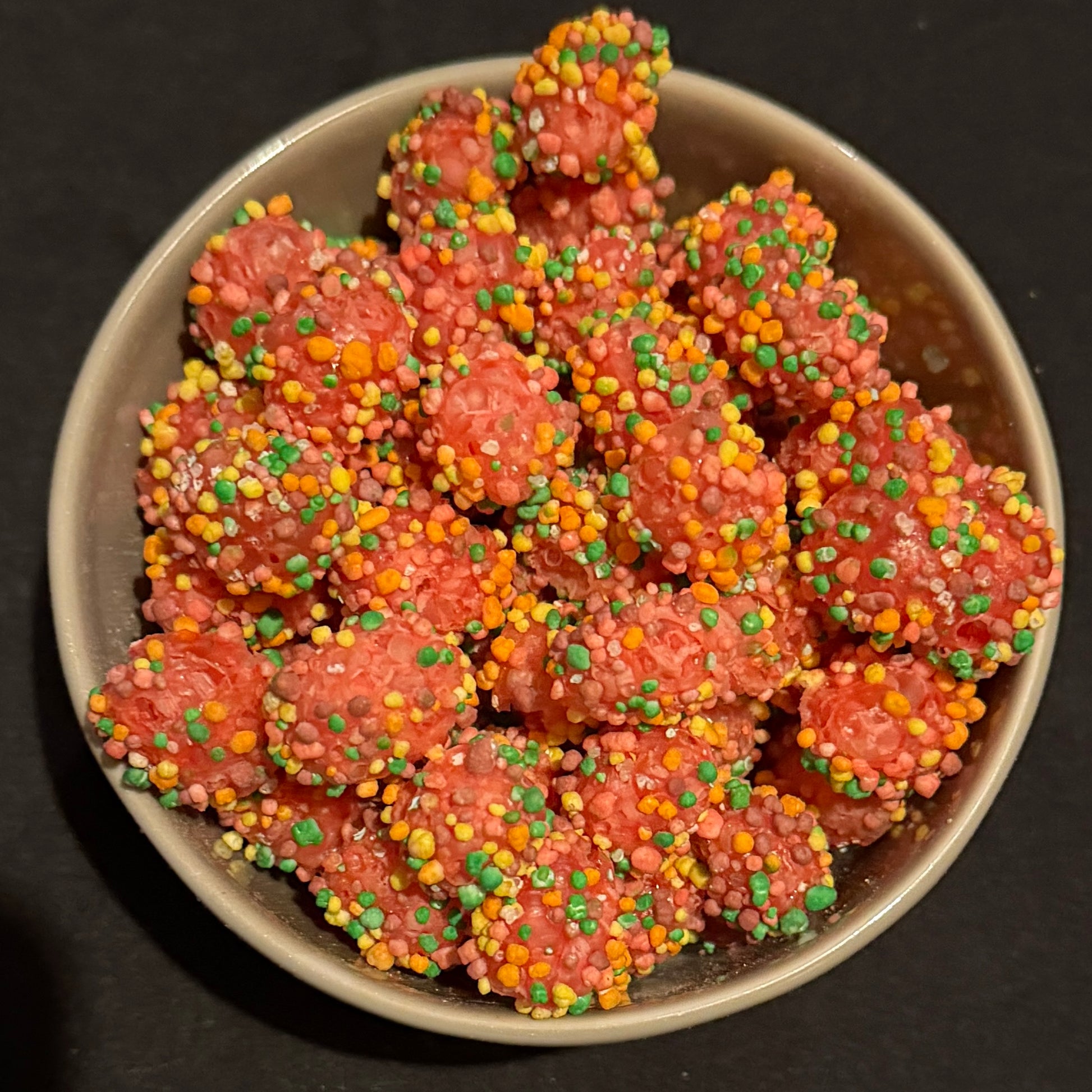 Pink freeze dried nerd gummy clusters with rainbow sprinkles in a dark grey bowl